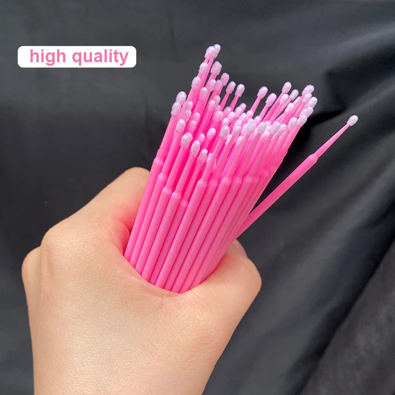 Une main tient un faisceau de pinceaux de nettoyage et d'extension pour cils roses.