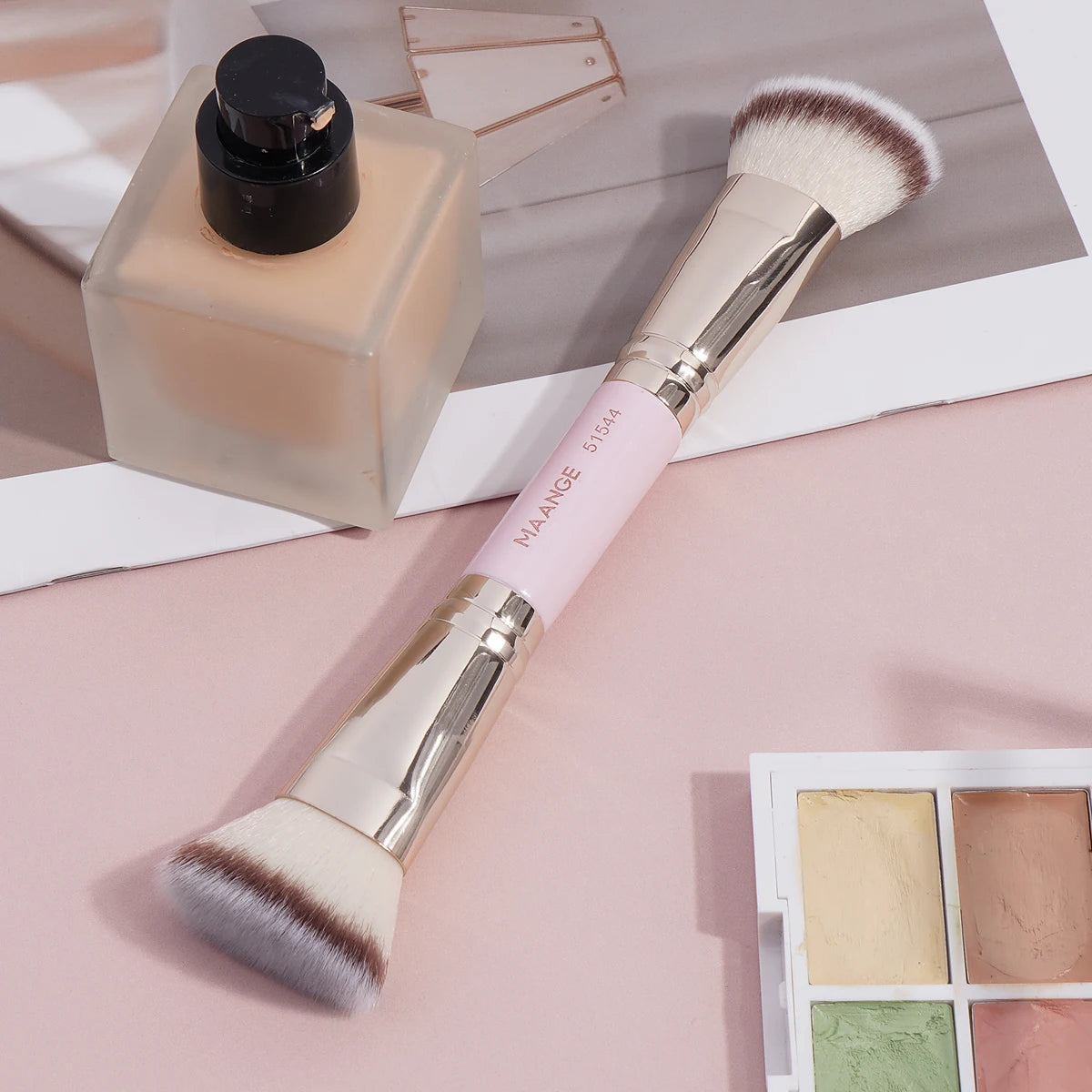 A makeup brush with a silver handle and fluffy bristles is shown next to a glass bottle of product.