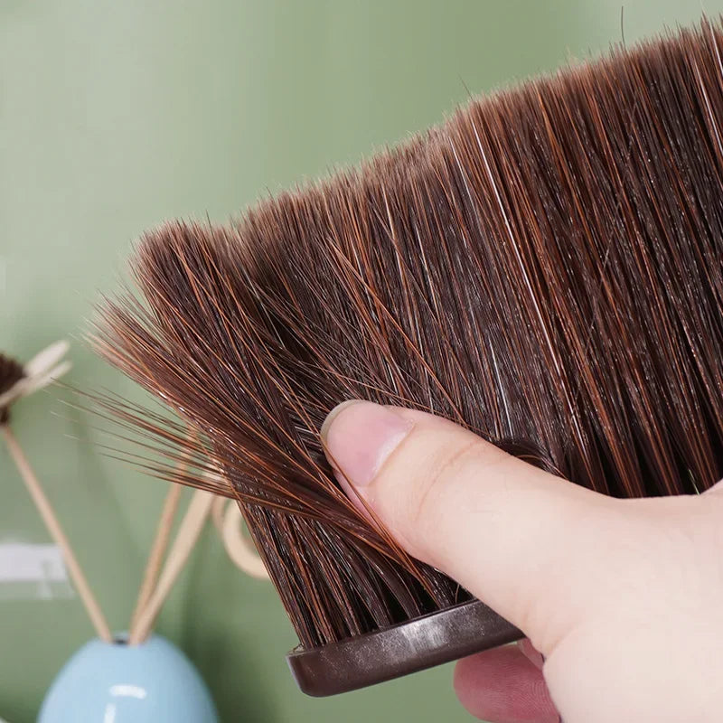 A hand holds a dark brown soft bristle hair duster brush, showing the bristles and handle.