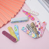 A collection of colorful double-sided nail files and buffing blocks arranged on a pink surface.