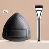 An XL triangular cosmetic foundation puff brush with a silver handle is shown on a light surface.