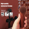 A hand holds a brown silicone facial cleansing brush against a reddish-brown tiled wall, demonstrating its waterproof design.