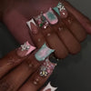 A hand displaying a set of nude pink press-on nails decorated with leopard print accents and 3D silver charms.