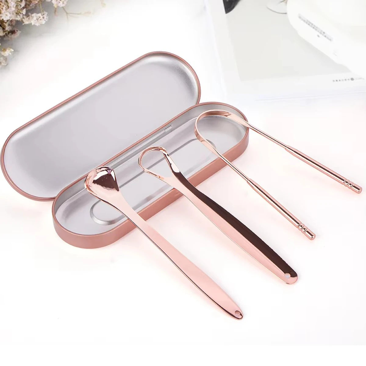 A set of rose gold stainless steel tongue scrapers in a rectangular case.