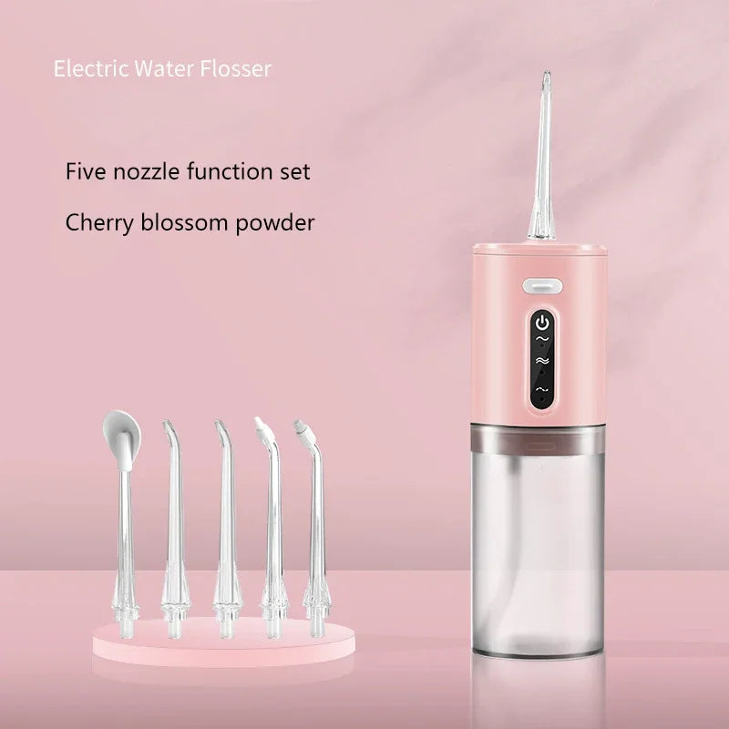 A pink electric water flosser with a silver body and five nozzle tips is displayed on a light pink surface.