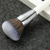 A silver and white professional makeup brush with a dense, fluffy bristles is shown on a dark gray surface.