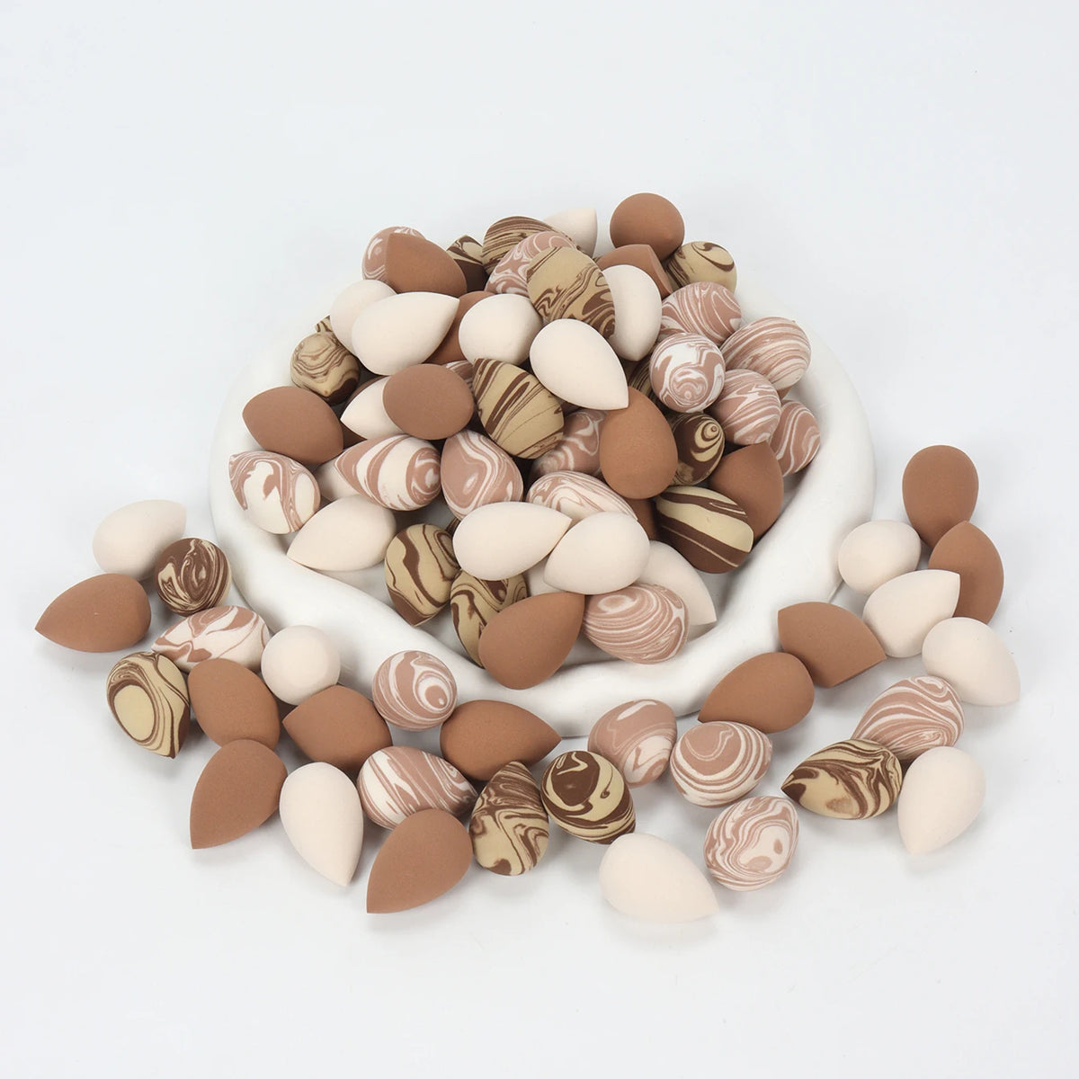 A pile of reusable expandable makeup sponges in various natural and earth tones.