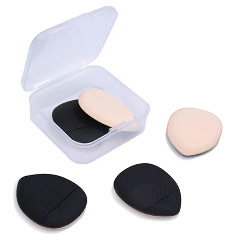 Un contenant en plastique transparent avec une éponge de fond de teint rose pâle et deux éponges de fond de teint noires.