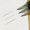 A close-up of an ultra-fine liquid eyebrow pen with a metallic tip and several lines of product on white paper.