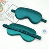 Two emerald green silk sleep eye masks with ruffled edges are displayed on a white surface.