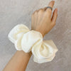 Une main attache un tissu de mousseline satinée blanche dans un élastique pour cheveux froncé.