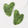 A green jade gua sha tool for facial lifting and muscle relaxation resting on a white surface.