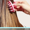 Une main utilise une brosse en silicone rose pour masser les cheveux et le cuir chevelu pendant une routine de soins capillai