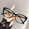 A hand holds a pair of black cat eye reading glasses against a light background.