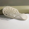 A white mini travel hair brush with numerous fine bristles is shown lying on a white surface.