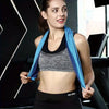 A woman wearing a black sports top and dark bottoms holds a blue towel in a gym setting.