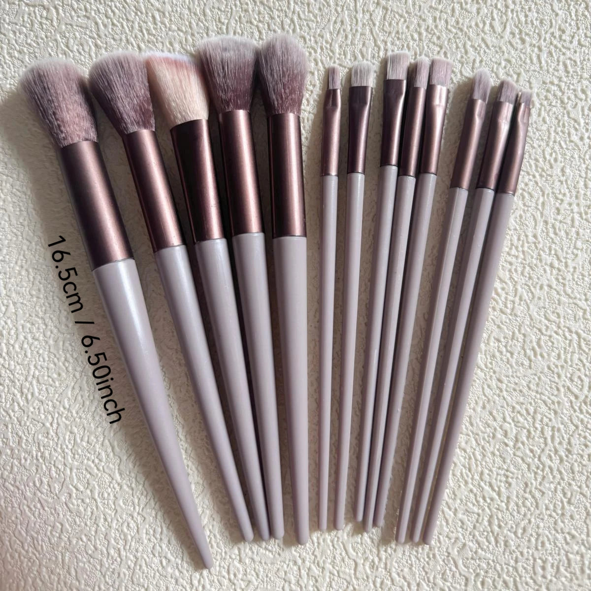 A set of professional makeup brushes in various shades of pink and nude are displayed on a light background.