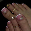 A close-up of a hand displaying press-on fake nails with a short square French design featuring pink and gold floral accents.