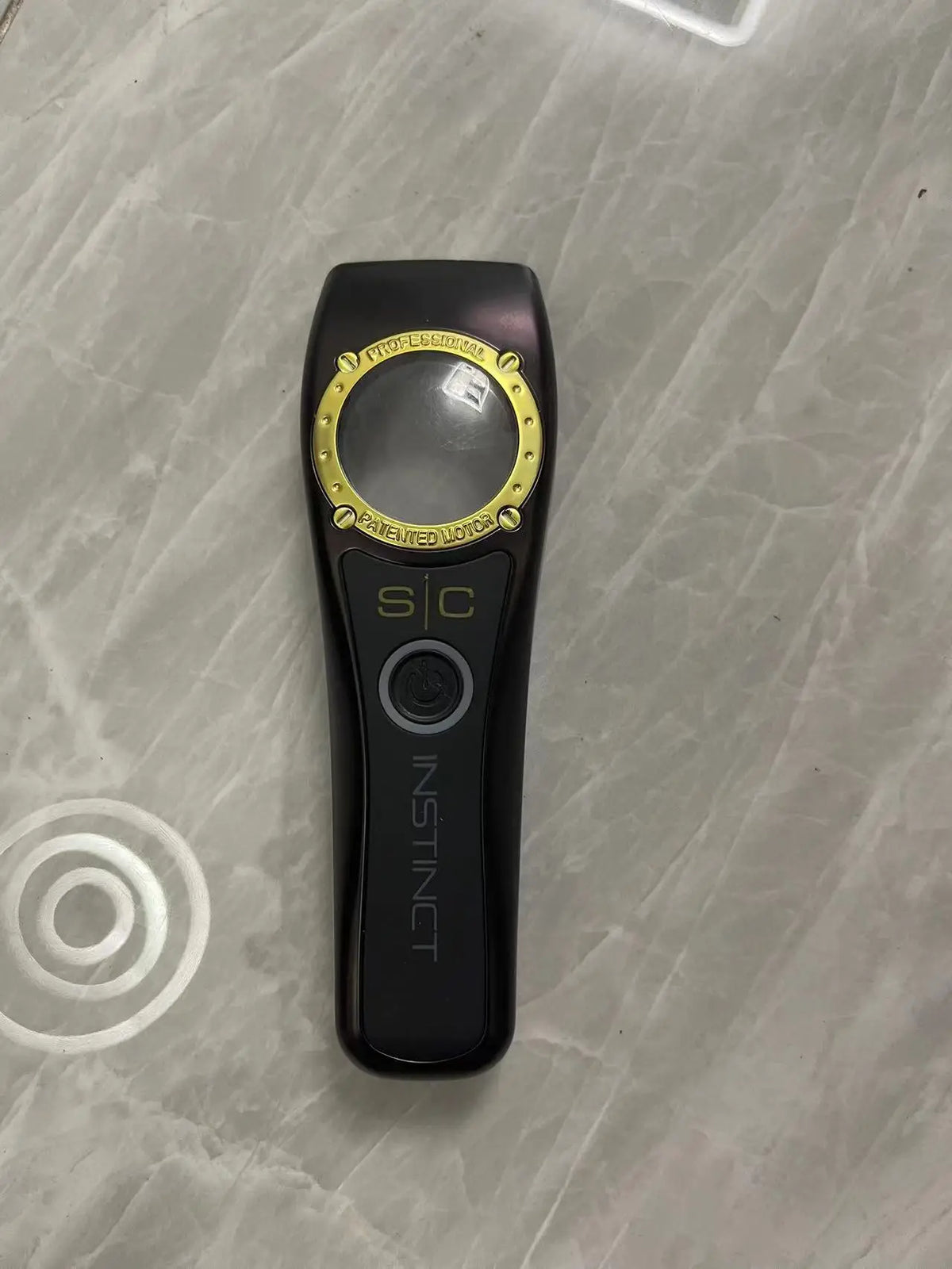A black professional electric hair trimmer with gold accents and an Instinct switch.