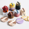 A collection of colorful beauty puffs and makeup applicators stacked in various shades on a white surface.