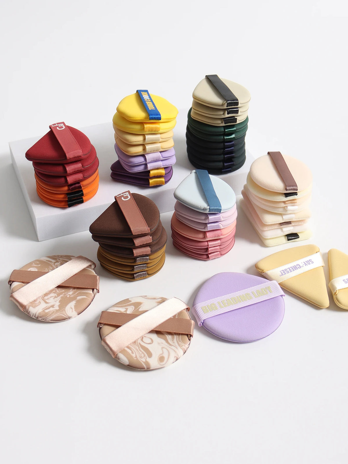 A collection of colorful beauty puffs and makeup applicators stacked in various shades on a white surface.