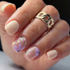 A hand models blue floral press-on false nails with gold accents and a gold link ring.