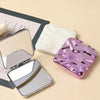 Miroir de maquillage carré pliable marbré rose et violet avec cadre argenté et tampon cosmétique blanc.
