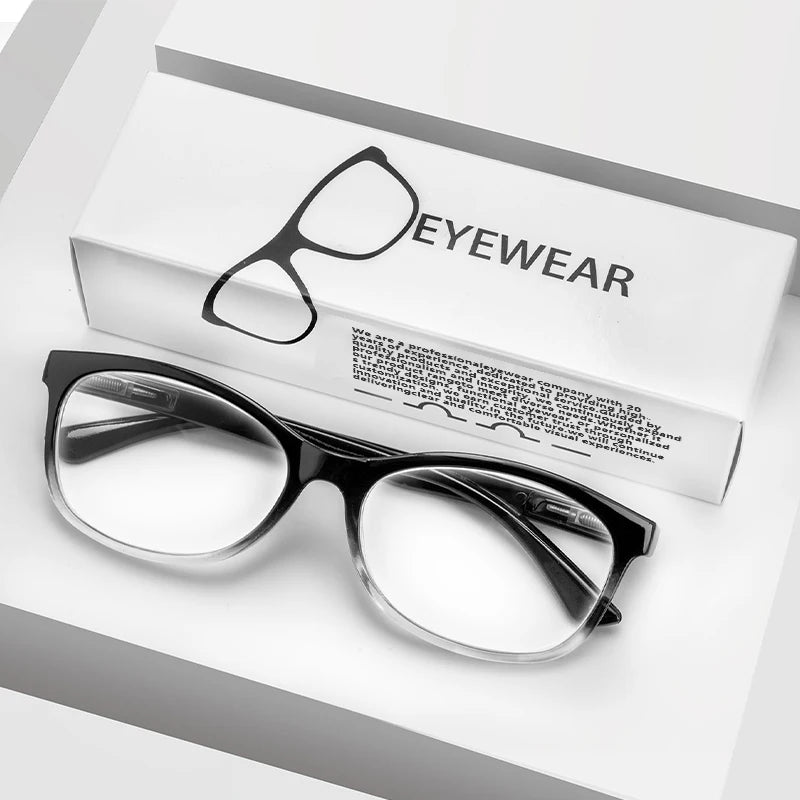 Une paire de lunettes de lecture avec des montures noires posée sur une boîte blanche marquée « EYEWEAR ».