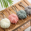 A collection of soft, exfoliating bath bubble balls in various shades of pink, green, and beige resting on a wooden tray.