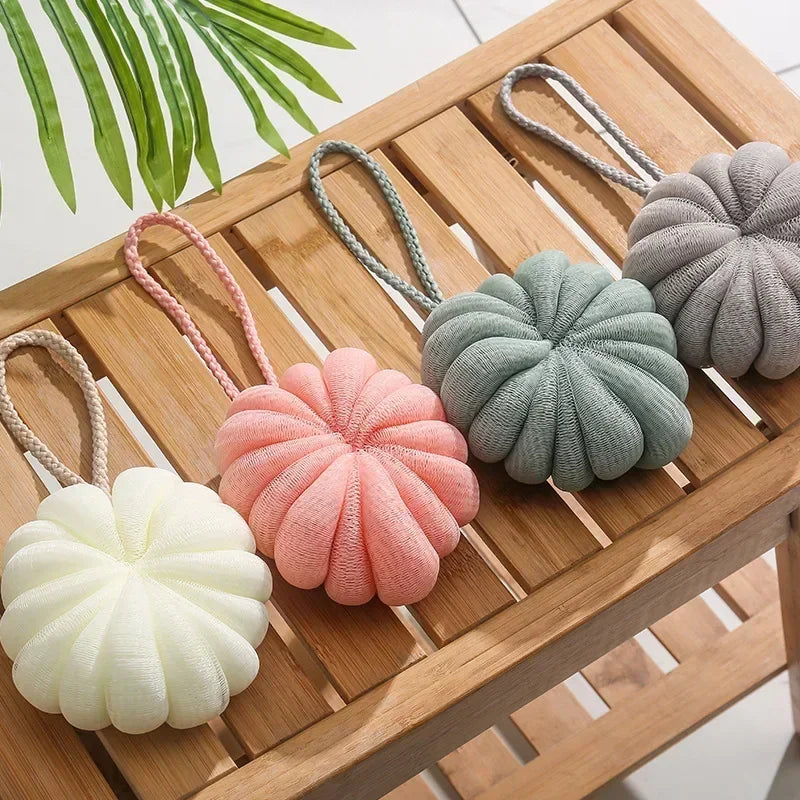 A collection of soft, exfoliating bath bubble balls in various shades of pink, green, and beige resting on a wooden tray.