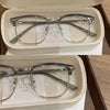 Un par de gafas con marco transparente y detalles plateados, exhibidas en una caja blanca.