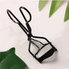 A black pro makeup eyelash curler is shown against a white background with green leaves.