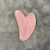 Un masajeador facial de cera rosa en forma de corazón sobre una superficie gris y peluda.
