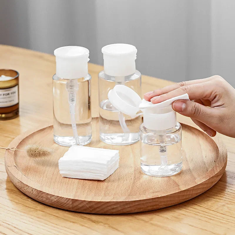 Three clear glass bottles with white pump dispensers are arranged on a wooden board.