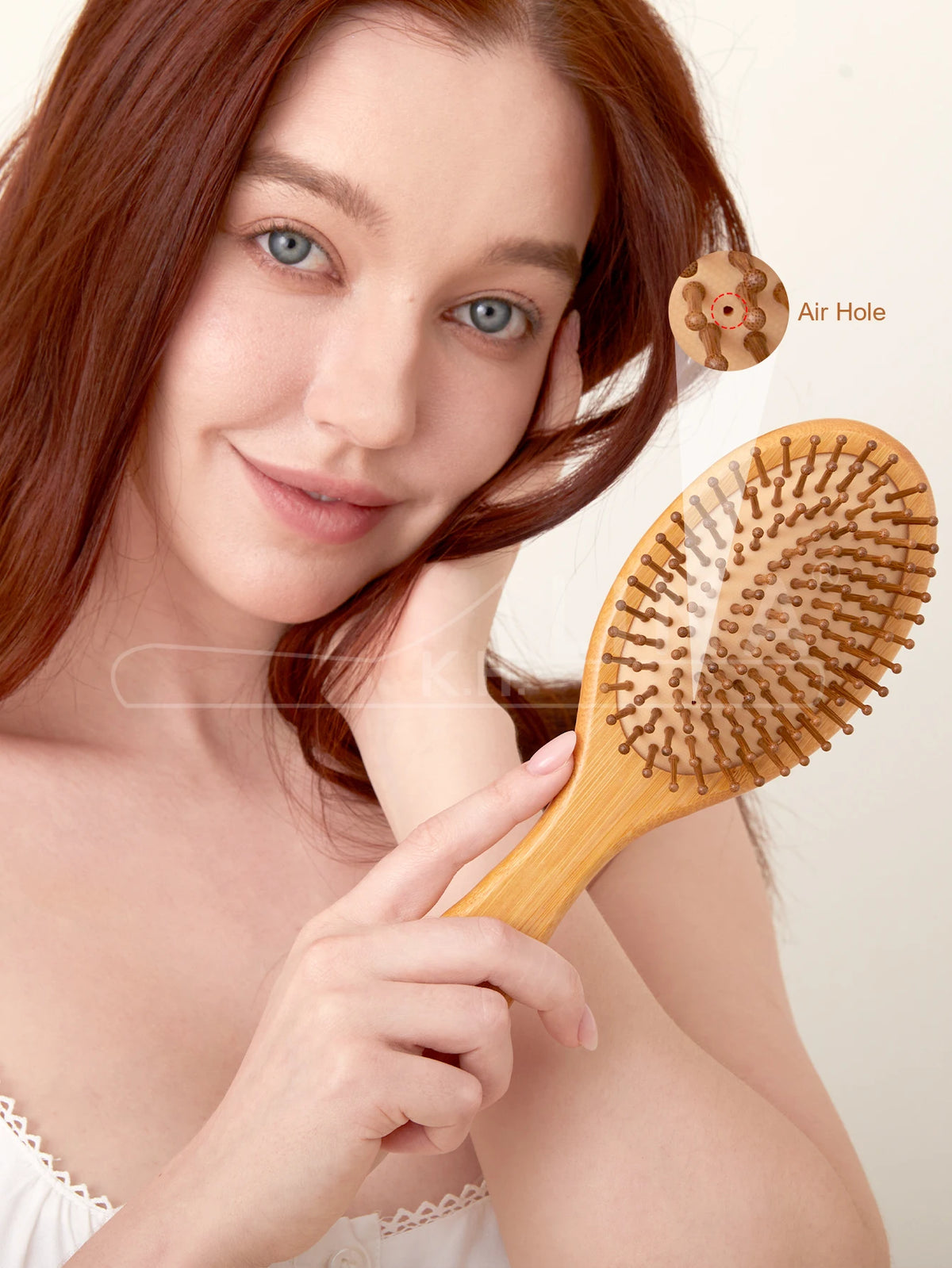 A woman is holding a wooden bamboo hair brush and pointing to an air hole on the brush.