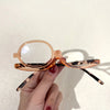 A hand holds a pair of rose gold tinted magnifying reading glasses with tortoiseshell accents.