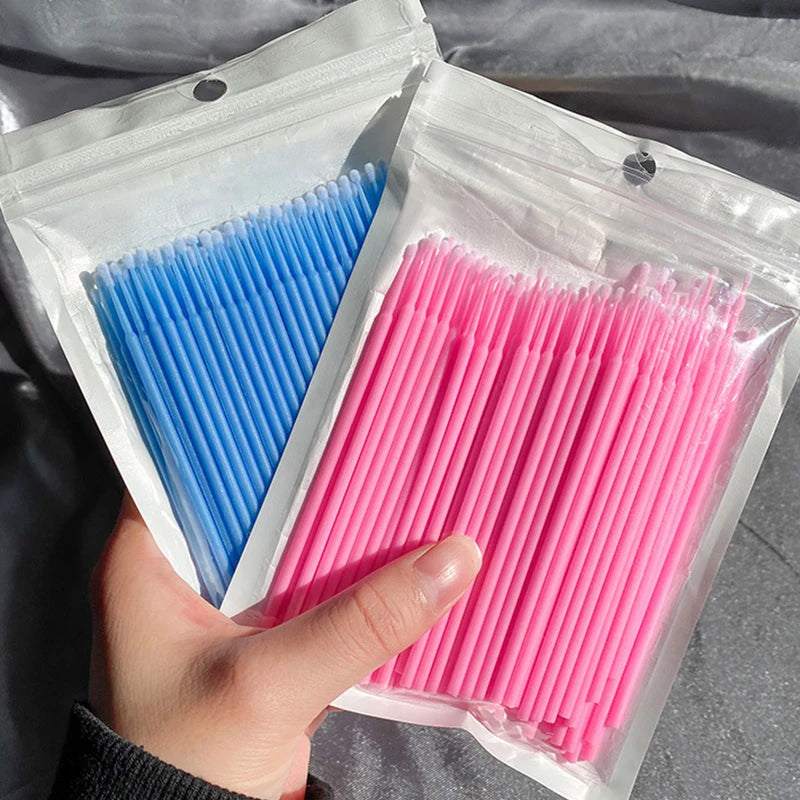 Une main tient un emballage plastique transparent contenant un paquet de pinceaux pour nettoyer et étendre les cils roses.