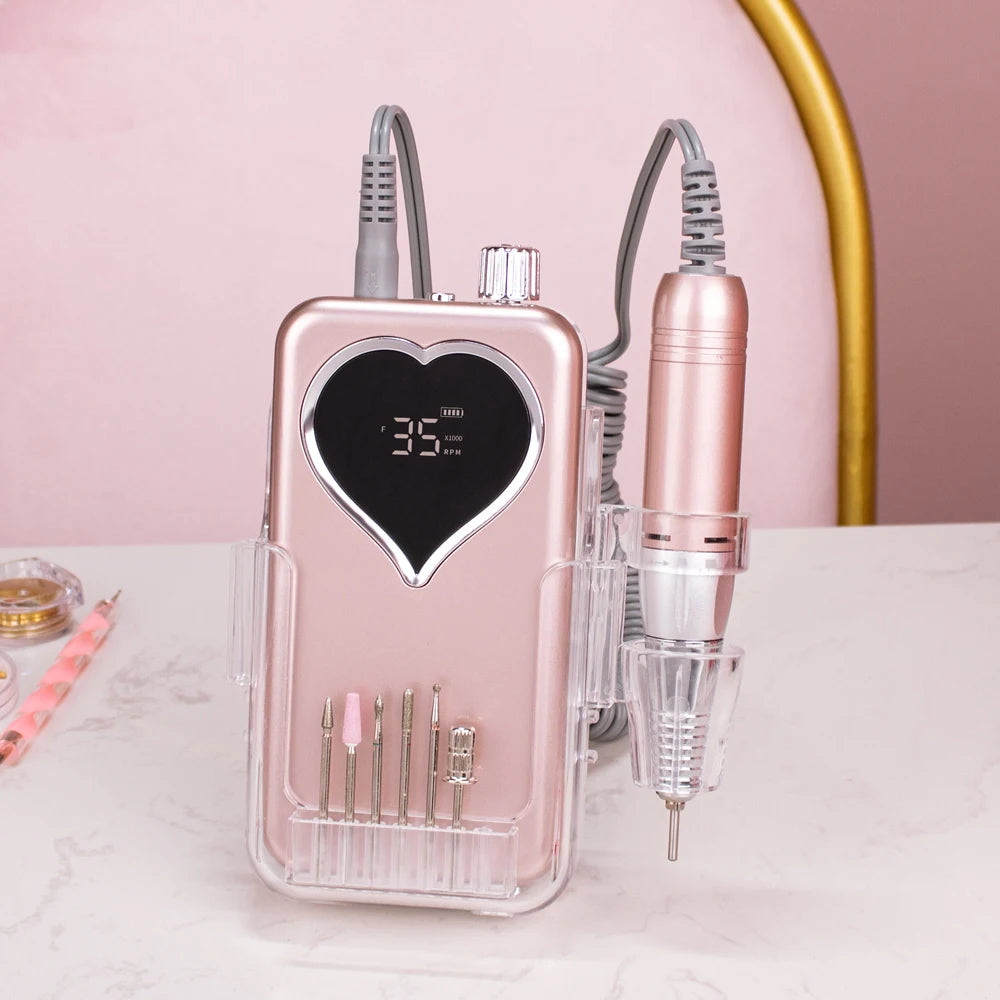 A pink cordless rechargeable nail drill with a heart-shaped body and various drills visible on the front.