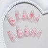 A collection of 24 press-on nails featuring pink flowers on a sheer, milky pink background.