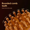 A close-up of a wooden rounded comb with numerous teeth, used for scalp massage.