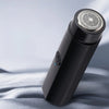 A black portable electric shaver with a mesh head is shown against a soft, light gray background.