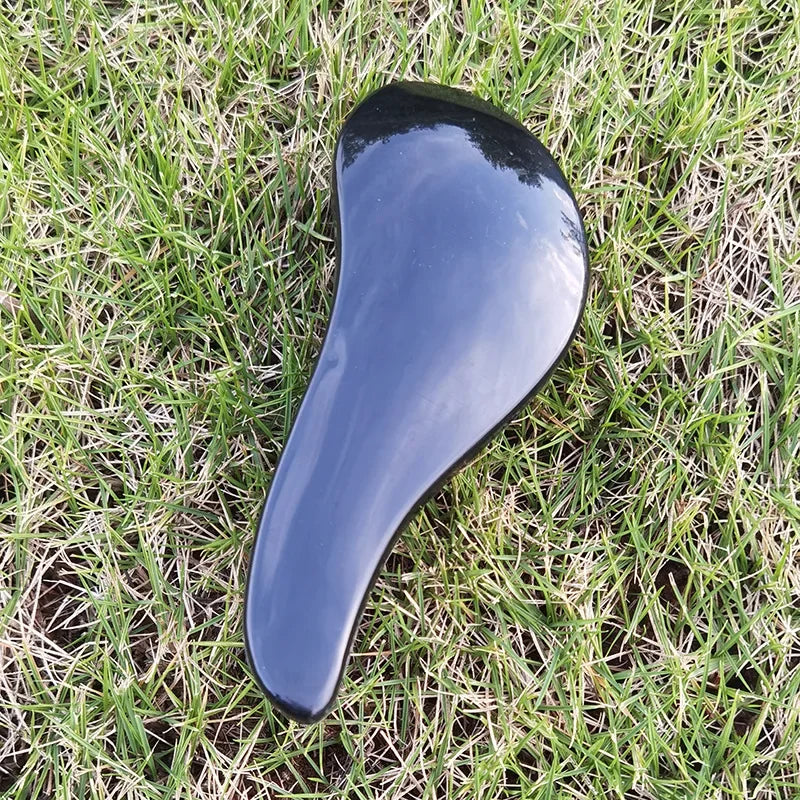 A smooth, dark blue silicone detangling hair brush lying on green grass.