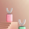 A pink electric toothbrush with a white head is displayed on a light wooden step, next to a green one.