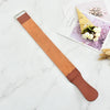 A brown leather sharpening strop with a metal handle rests on a white marble surface next to a card.