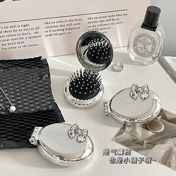 A set of silver folding massage combs and a makeup mirror displayed on a white surface.