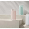 A collection of portable oral irrigators in pink and mint green are displayed on a light-colored shelf.