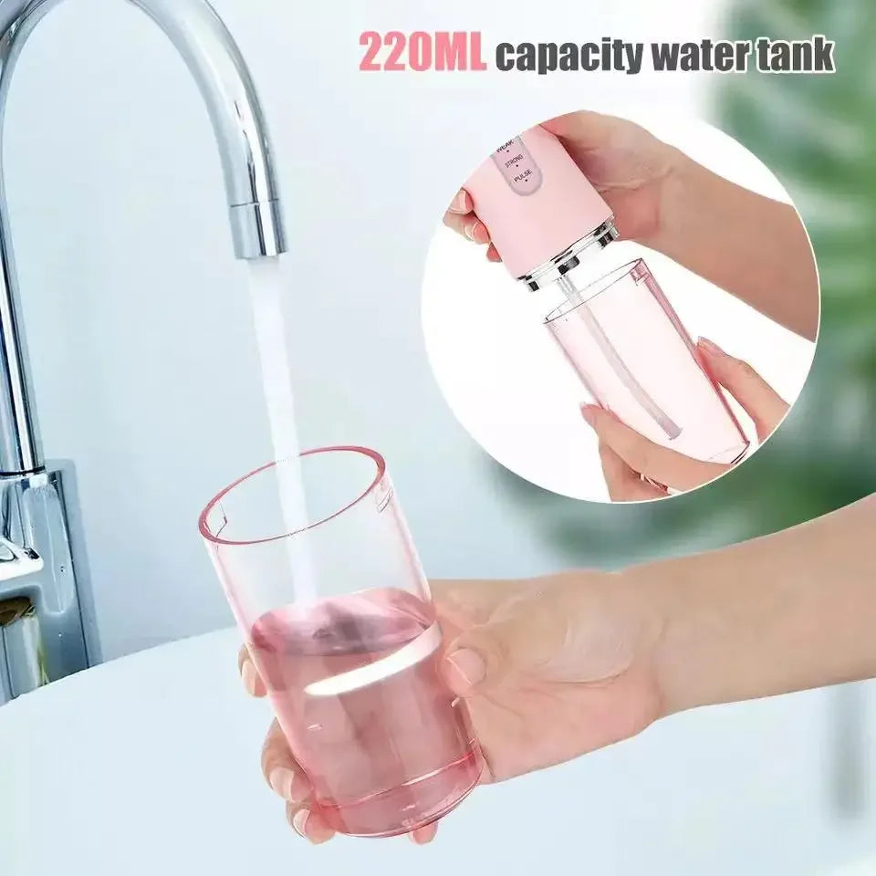 A hand is using a pink 220ml capacity water tank oral irrigator to flush water into a glass.