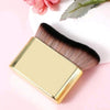 Un set de pinceaux de maquillage de couleur or avec des poils foncés est exposé sur un fond rose à côté d'une fleur.