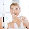 A woman is holding an electric dental calculus scaler and a toothbrush in a bright setting.