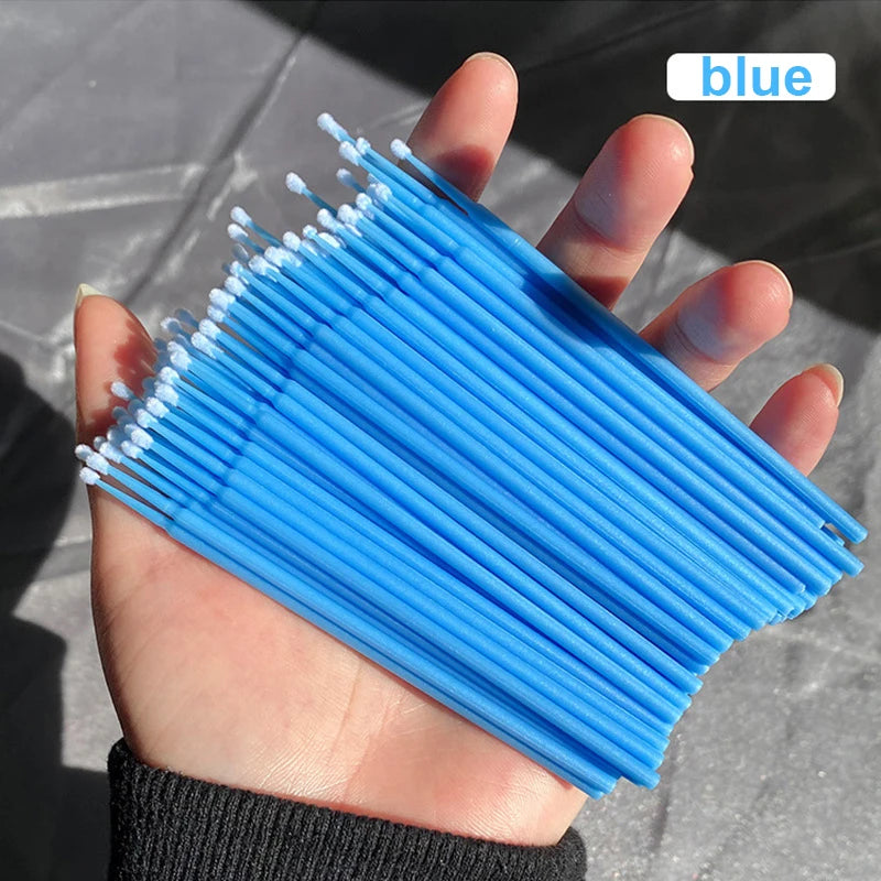 Une main tient un paquet de brosses pour nettoyer et étendre les cils bleus.